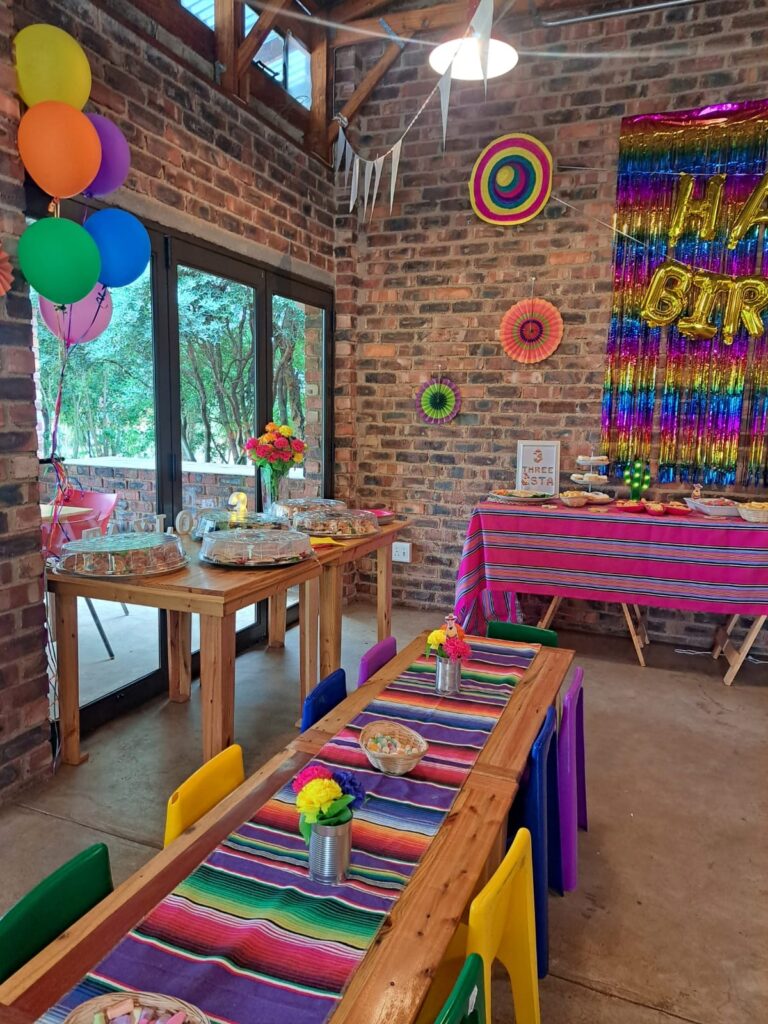 A colorful party setup at The Barn on Boundary in Johannesburg, featuring a vibrant table setting, balloons, and decorations.