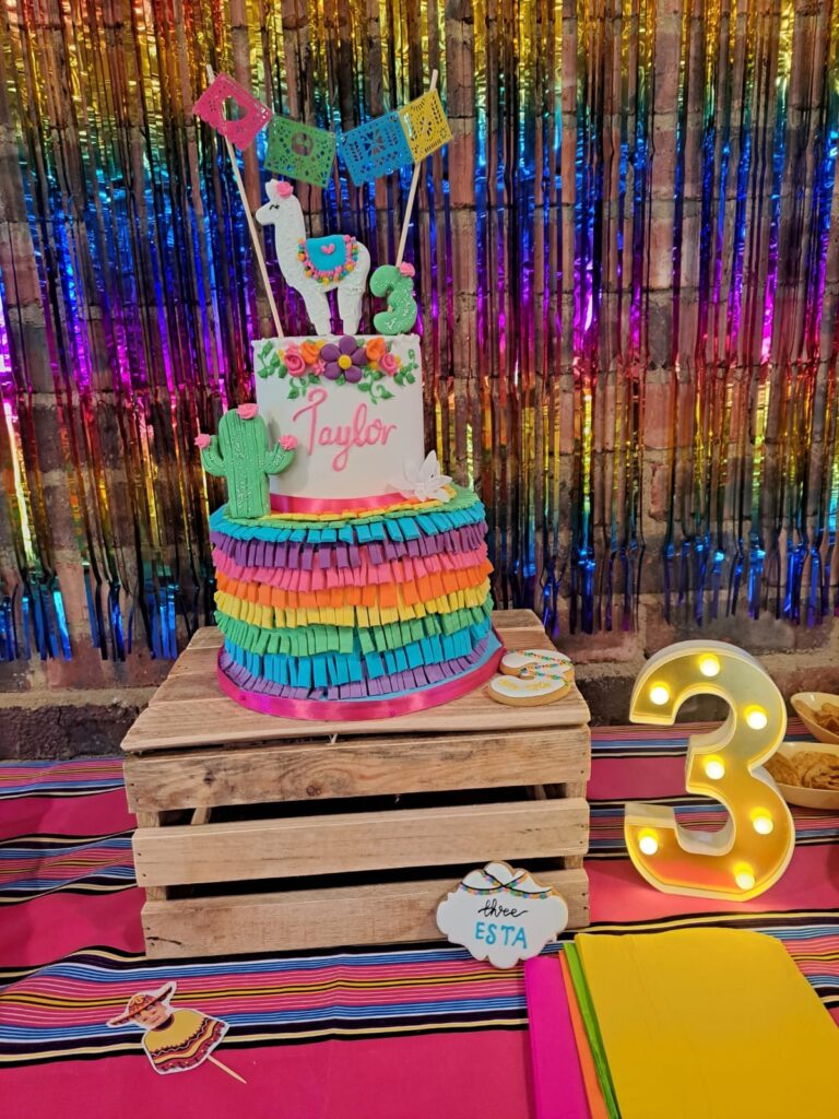 A colorful birthday cake with the name Taylor and a number 3 light sign on a table, set against a vibrant backdrop at The Barn on Boundary in Johannesburg, Northriding.
