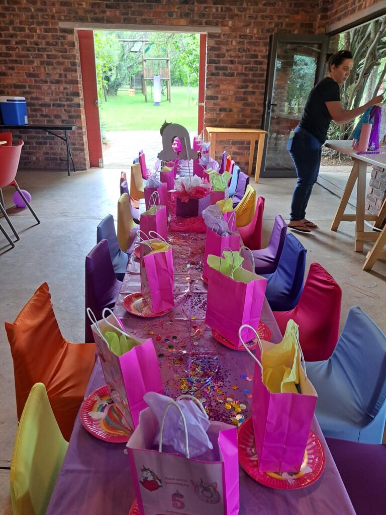 A colorful childrenβs party setup with decorated tables, gift bags, and a playground visible through the open door at The Barn on Boundary Party Venue in Johannesburg.