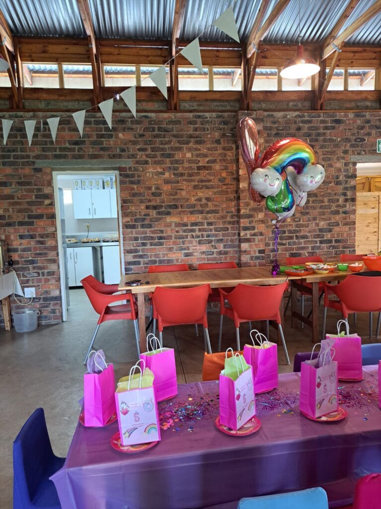 A colorful party setup at the Barn on Boundary Party Venue in Johannesburg, Northriding featuring pink gift bags, a unicorn balloon, and a festive table setting.