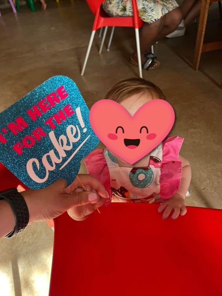A child at a party at The Barn on Boundary in Johannesburg, holding hands with an adult who is holding a sign that says βIβm here for the cake!β