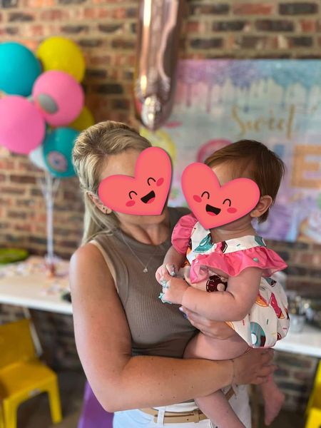 A person holding a child in front of a colorful party backdrop at The Barn on Boundary Party Venue.